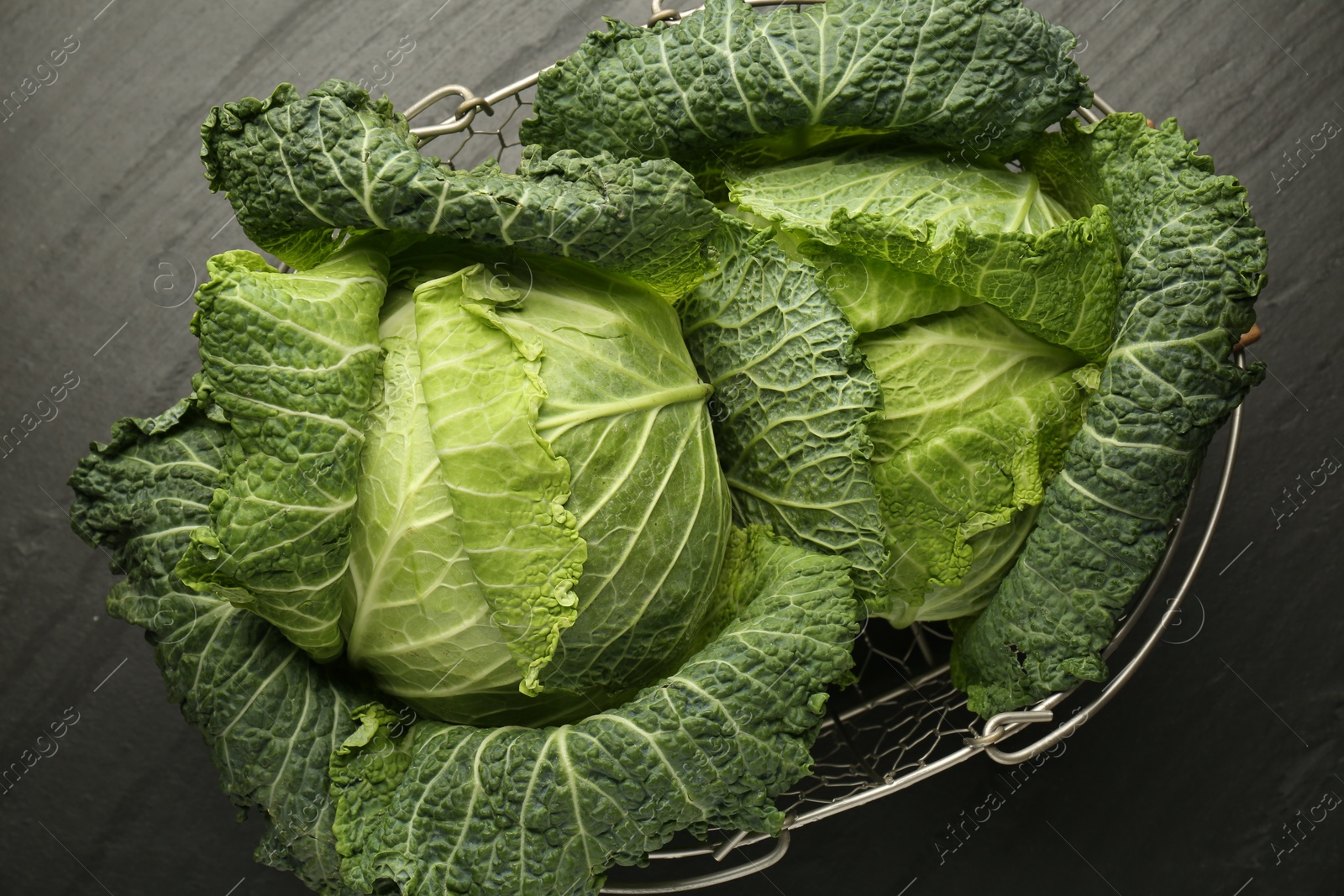 Photo of Fresh Savoy cabbages in metal basket on black table, top view