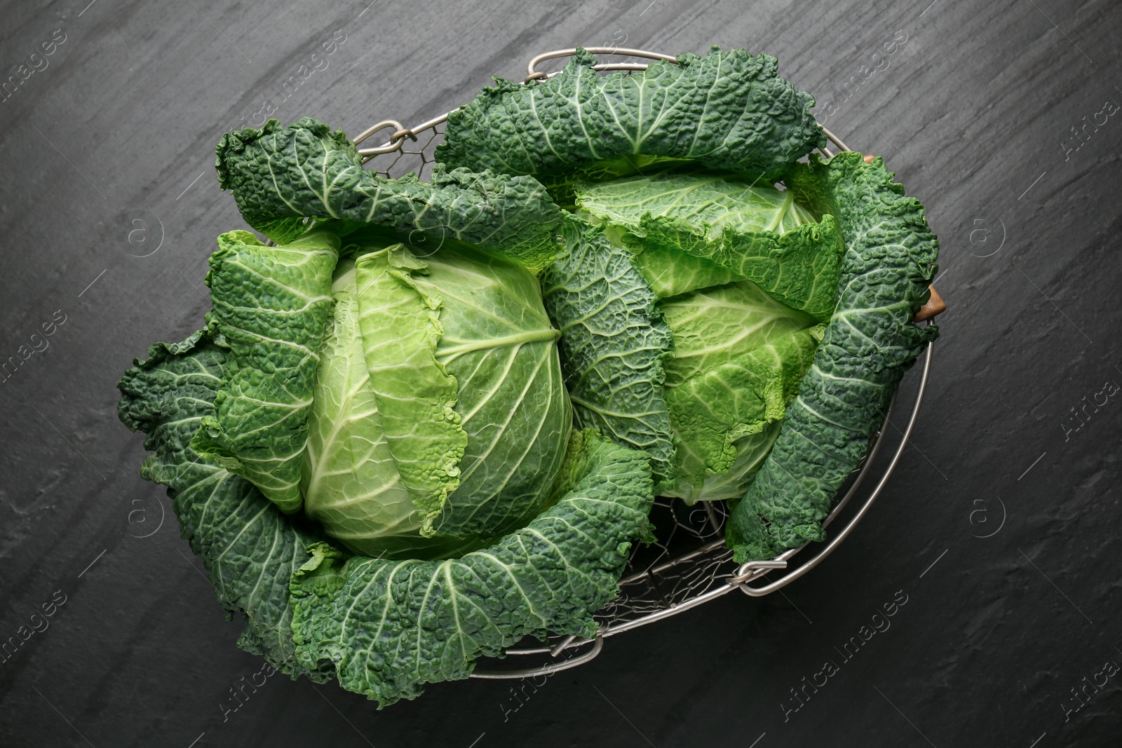 Photo of Fresh Savoy cabbages in metal basket on black table, top view