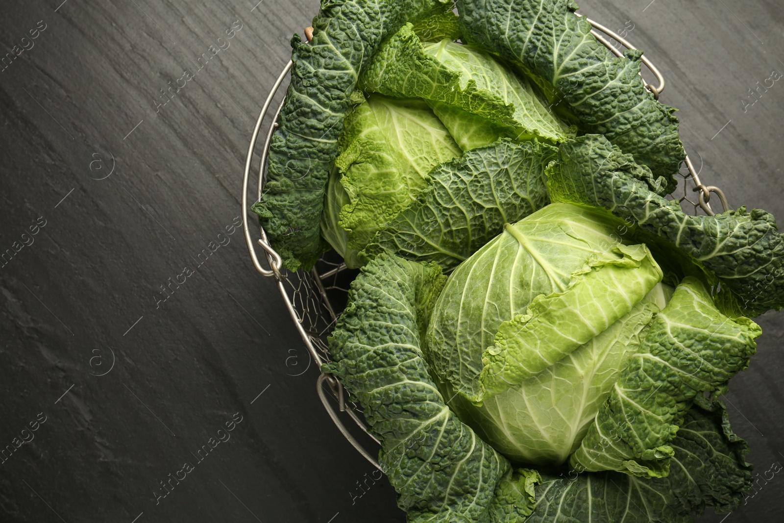 Photo of Fresh Savoy cabbages in metal basket on black table, top view. Space for text