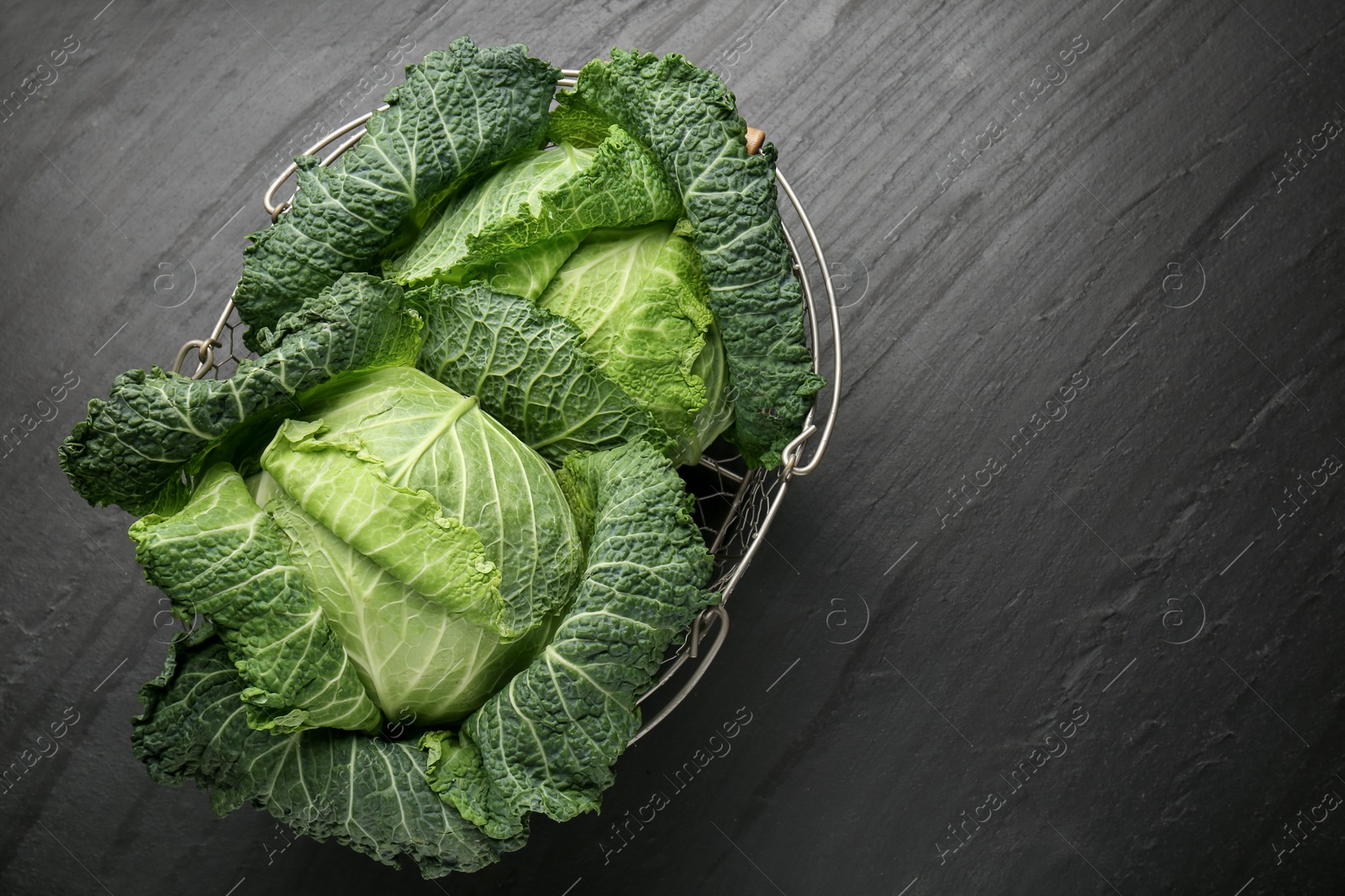 Photo of Fresh Savoy cabbages in metal basket on black table, top view. Space for text