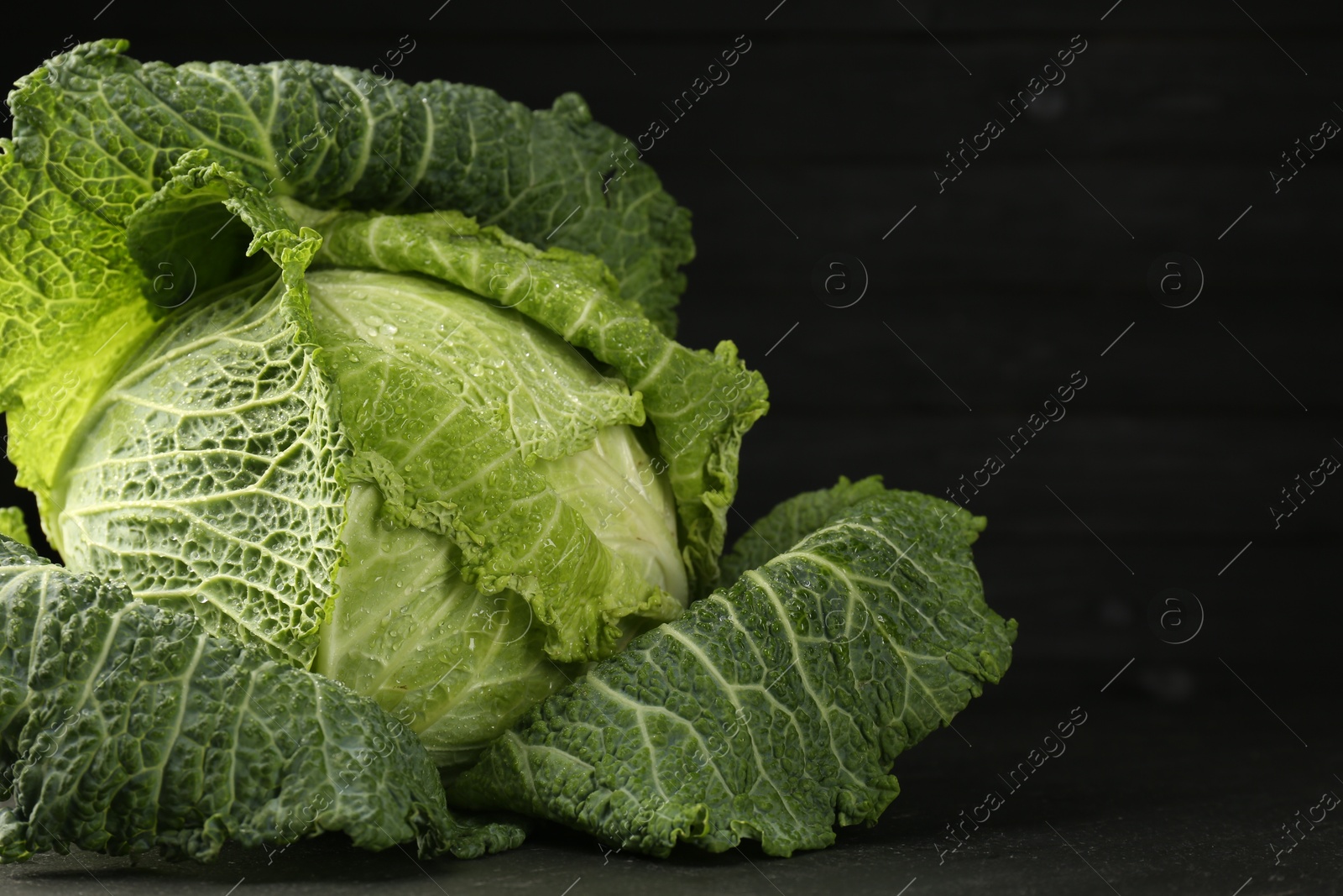 Photo of Fresh Savoy cabbage on black table, closeup. Space for text