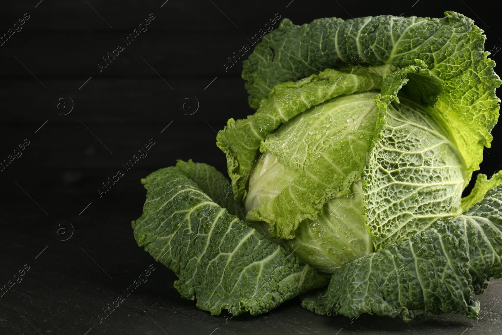 Photo of Fresh Savoy cabbage on black table, closeup. Space for text
