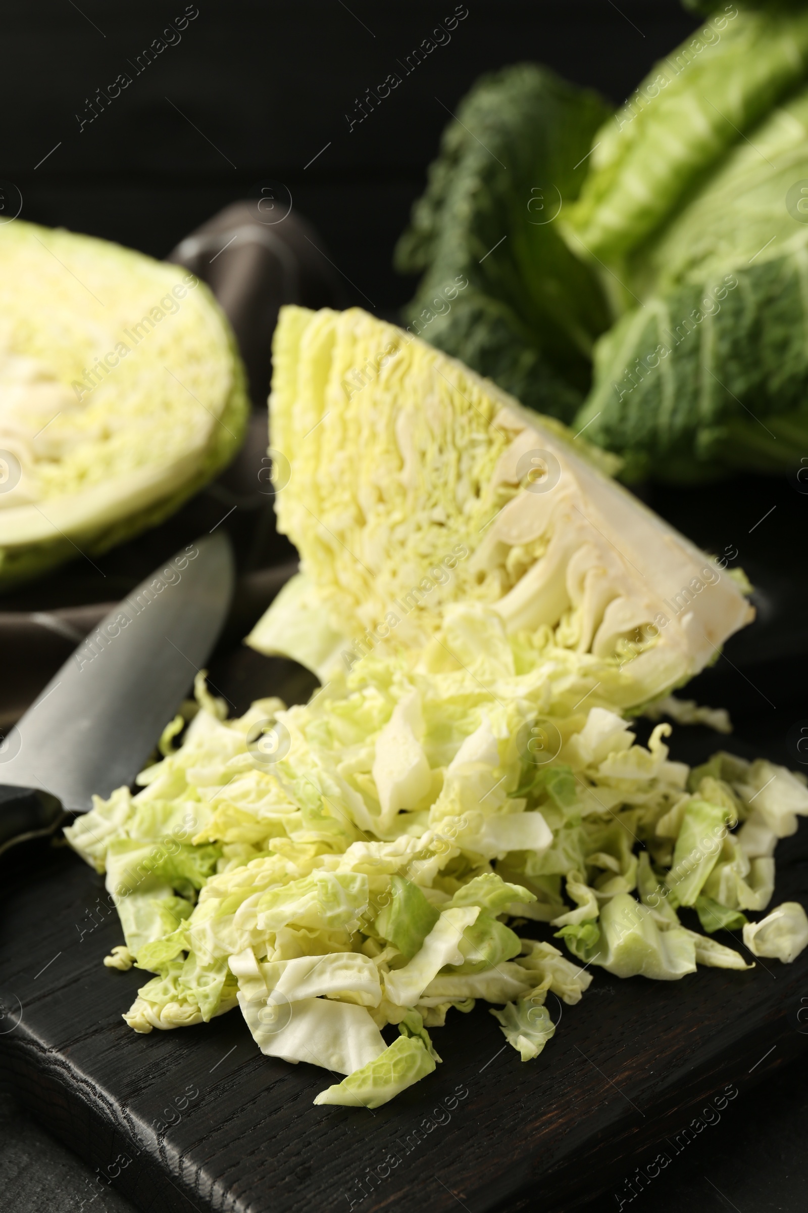 Photo of Shredded Savoy cabbage and knife on black table, closeup