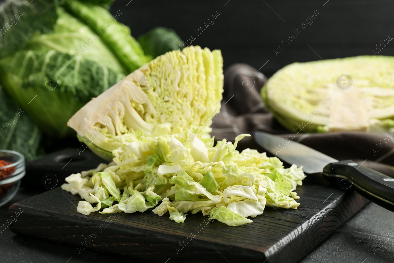 Photo of Shredded Savoy cabbage and knife on black table, closeup