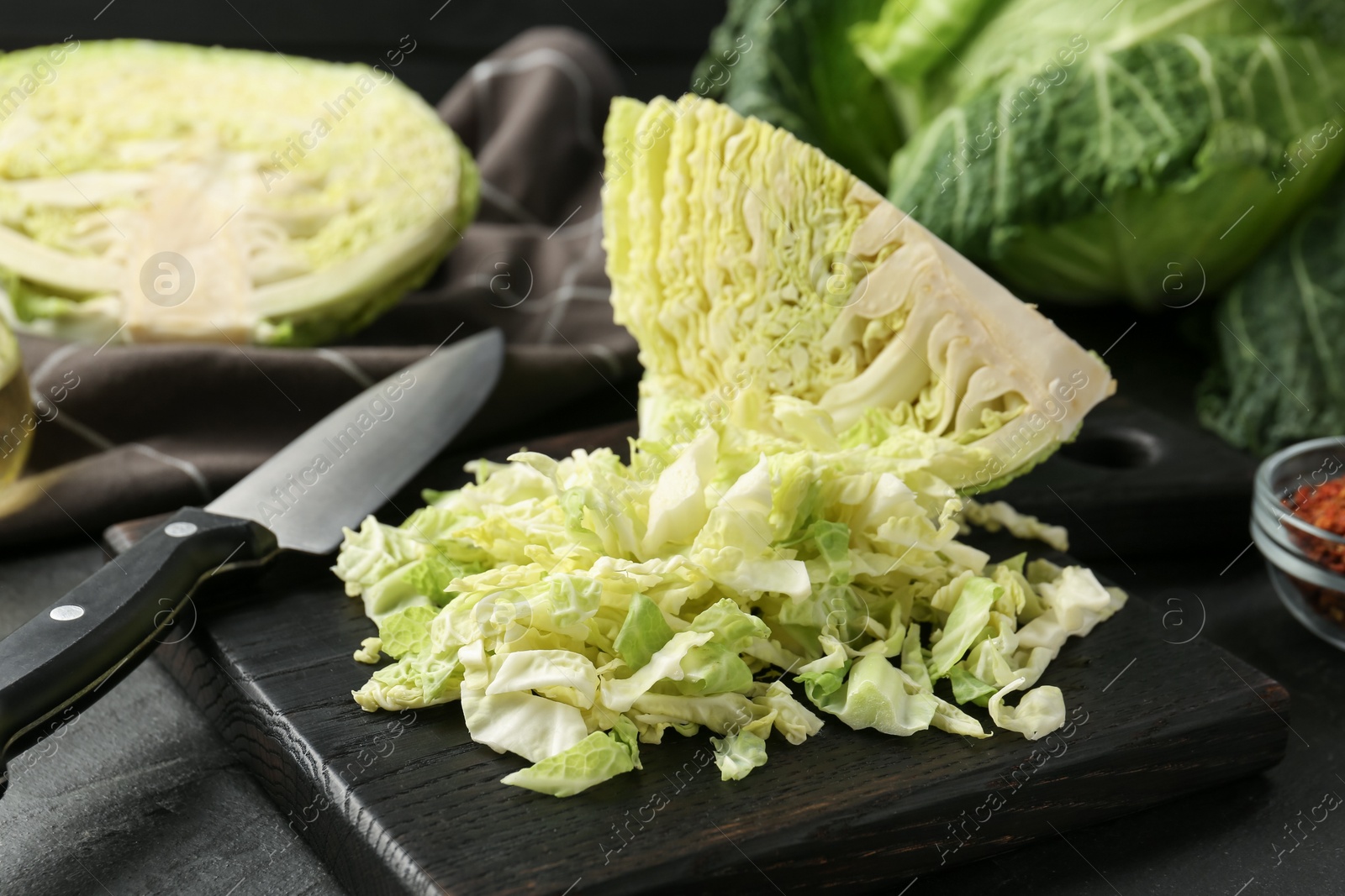 Photo of Shredded Savoy cabbage and knife on black table, closeup