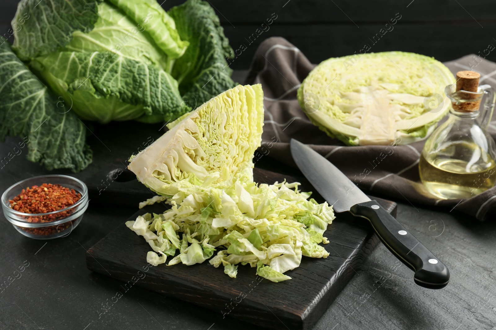 Photo of Fresh Savoy cabbages, spices, oil and knife on black table, closeup