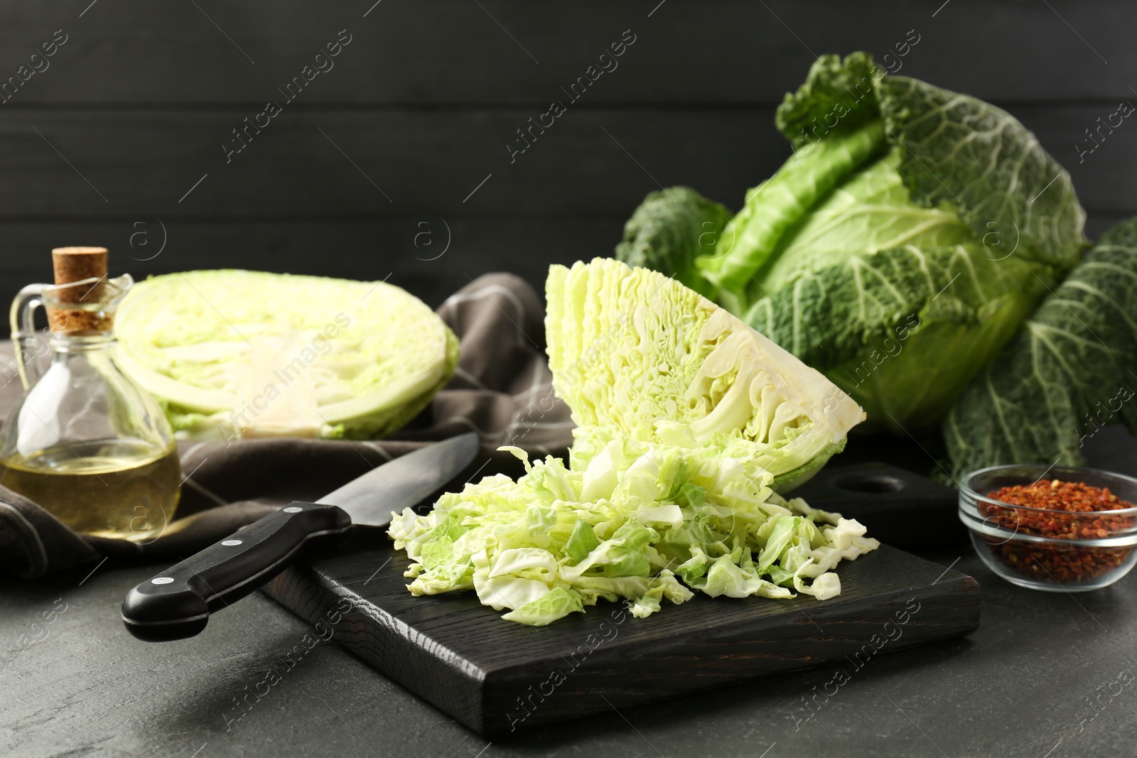 Photo of Fresh Savoy cabbages, spices, oil and knife on black table, closeup