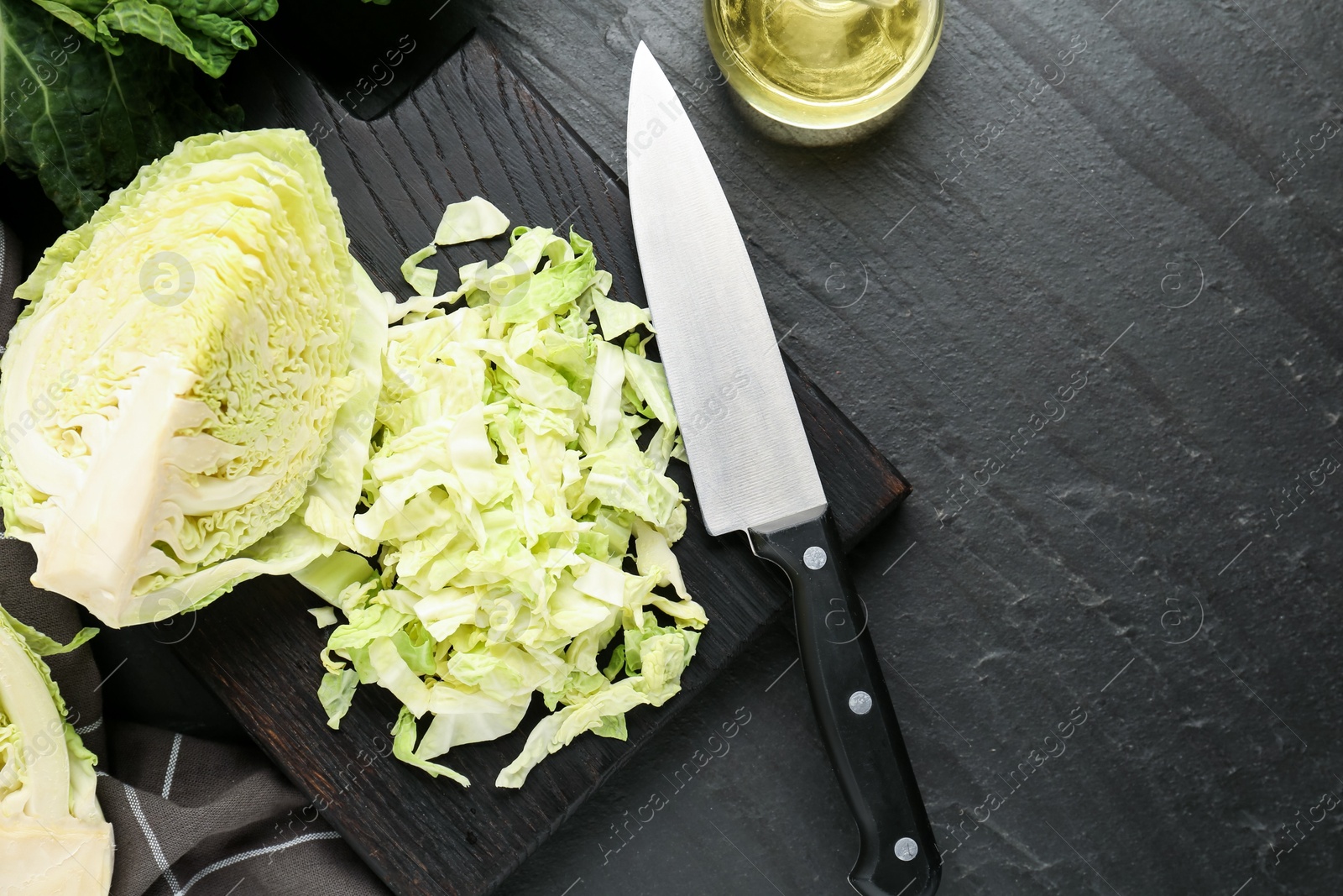 Photo of Cut fresh Savoy cabbage, spices, oil and knife on black table, flat lay. Space for text