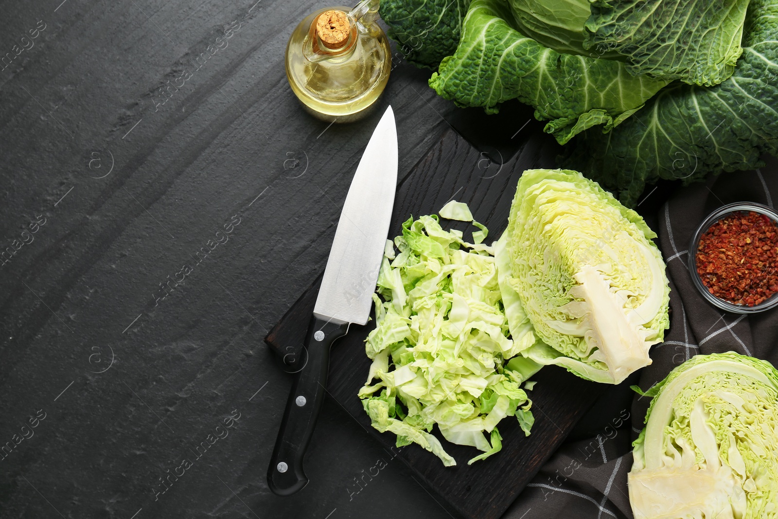 Photo of Cut fresh Savoy cabbage, spices, oil and knife on black table, flat lay. Space for text