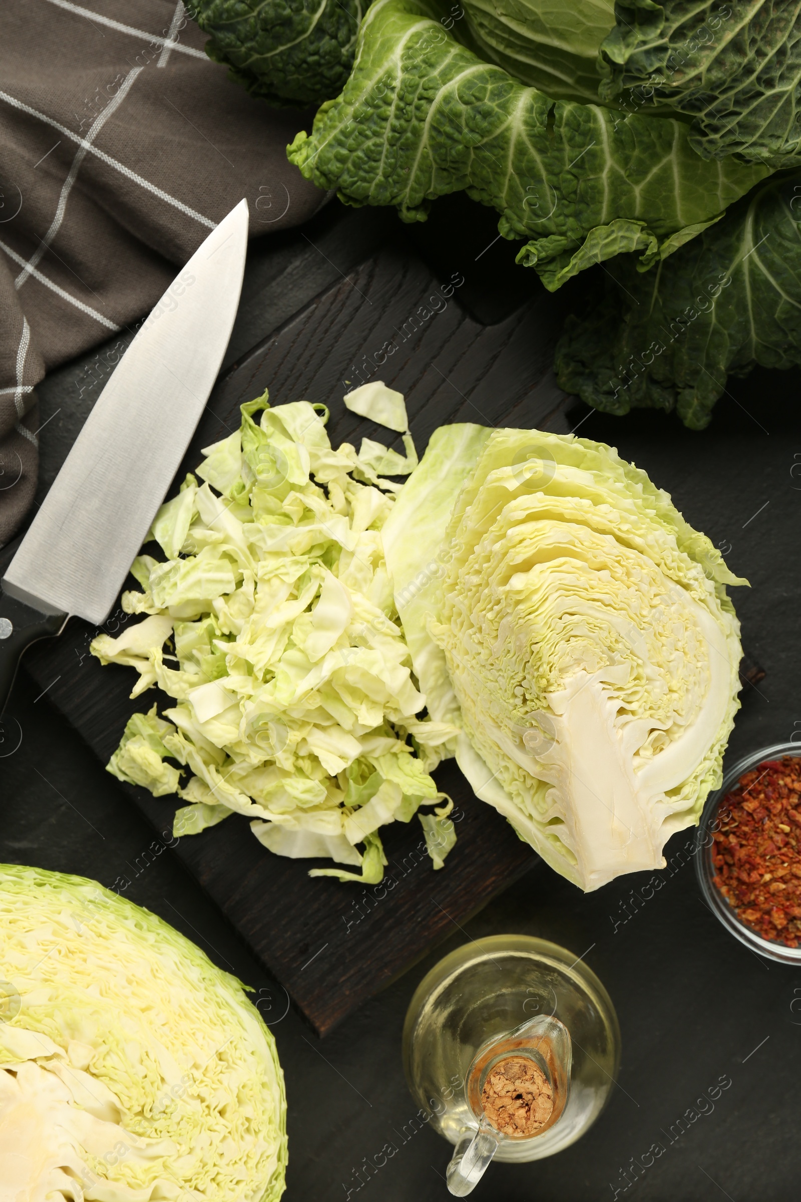 Photo of Cut fresh Savoy cabbage, spices, oil and knife on black table, flat lay