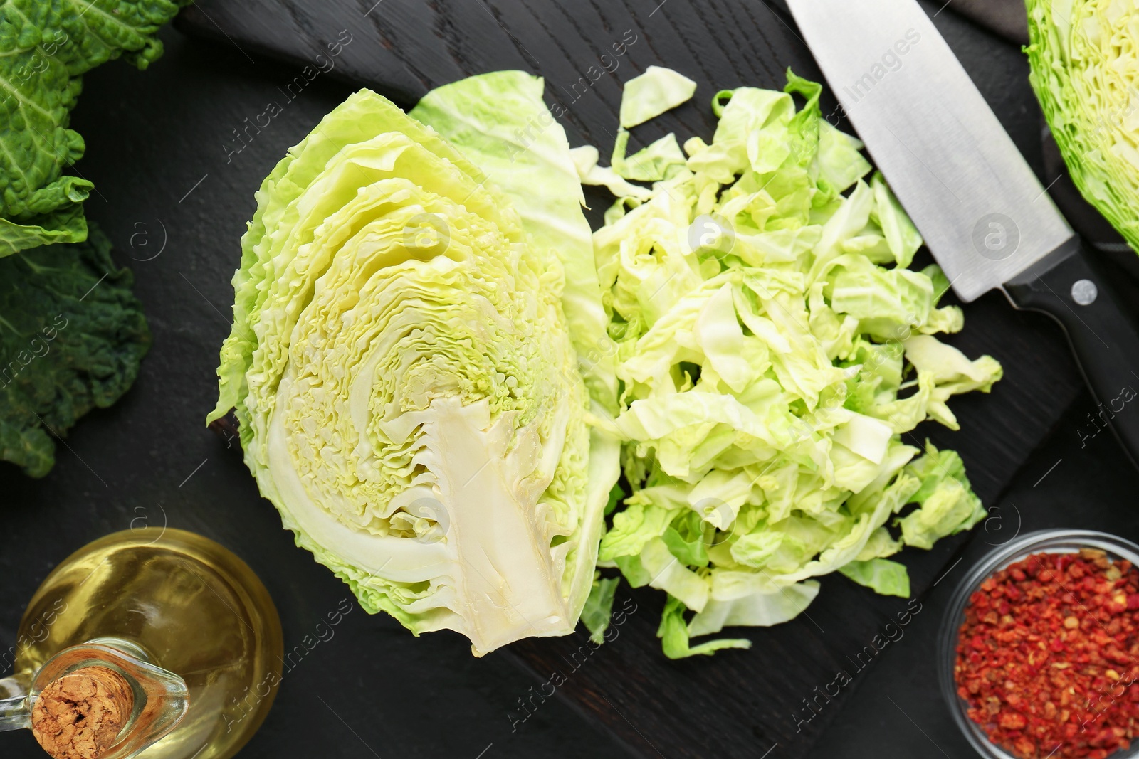 Photo of Cut fresh Savoy cabbage, spices, oil and knife on black table, flat lay