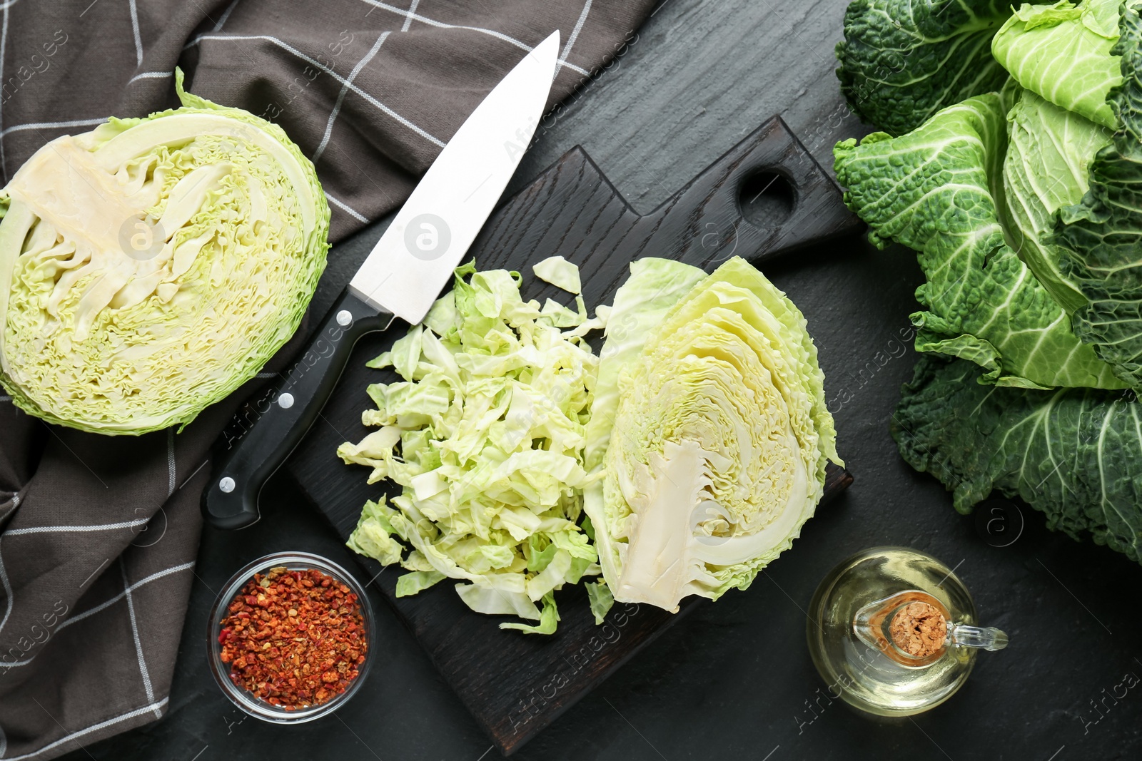 Photo of Cut fresh Savoy cabbage, spices, oil and knife on black table, flat lay
