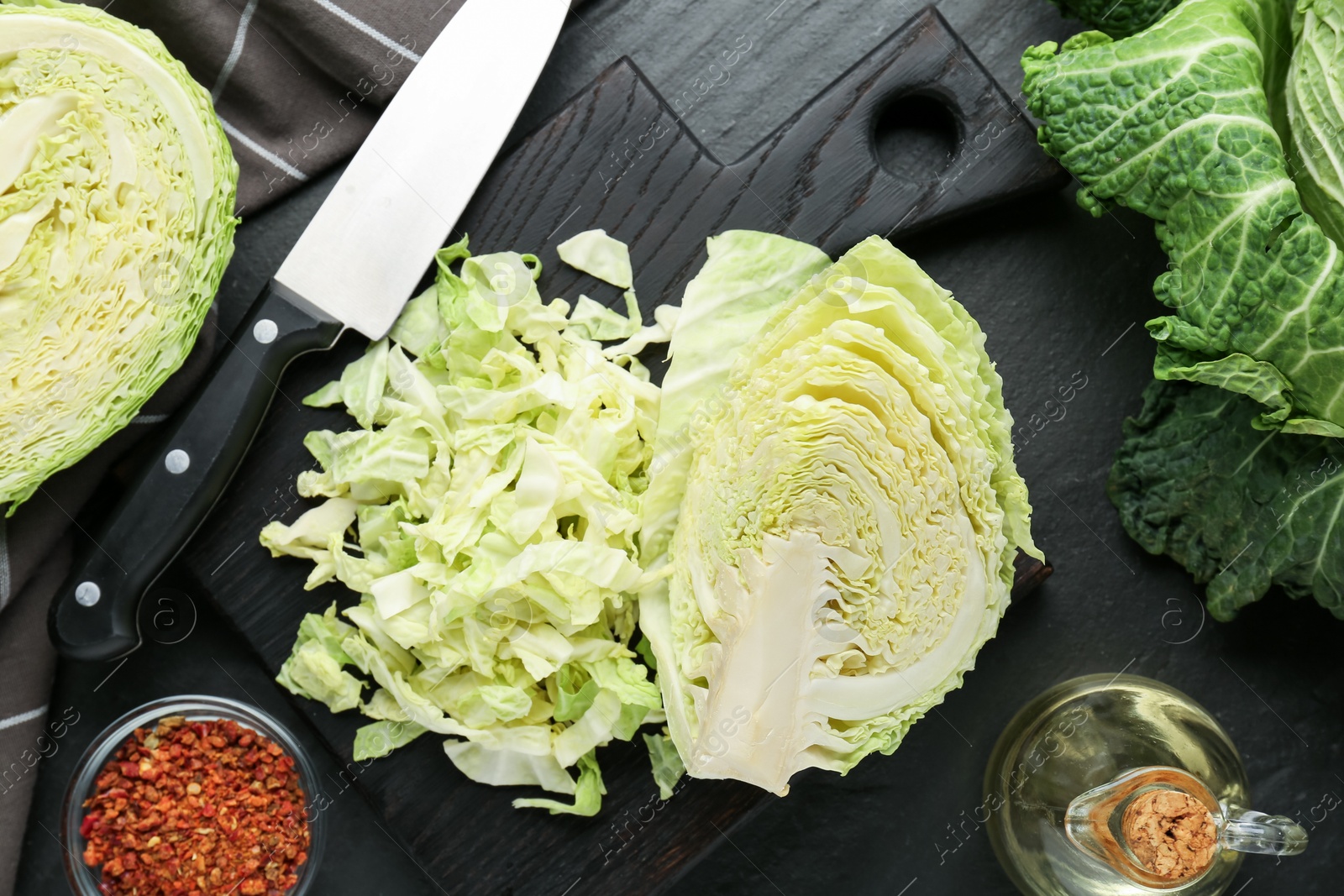 Photo of Cut fresh Savoy cabbage, spices, oil and knife on black table, flat lay