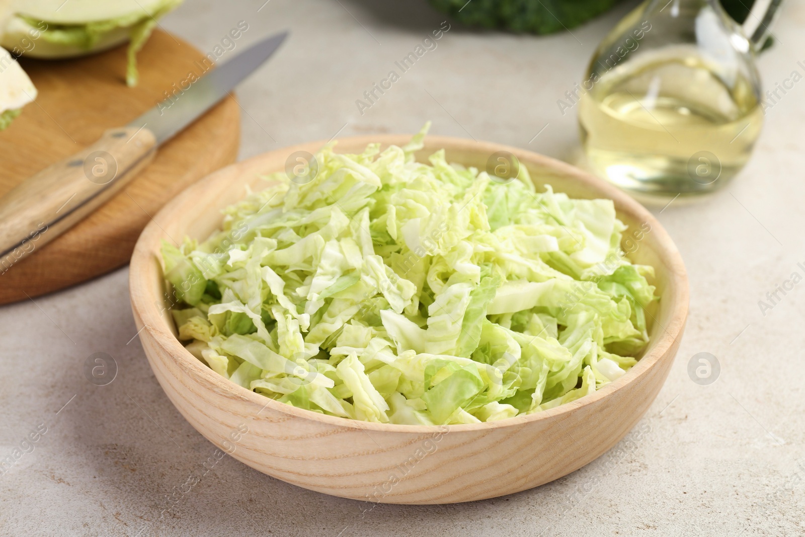 Photo of Shredded Savoy cabbage in bowl, knife and oil on light table, closeup