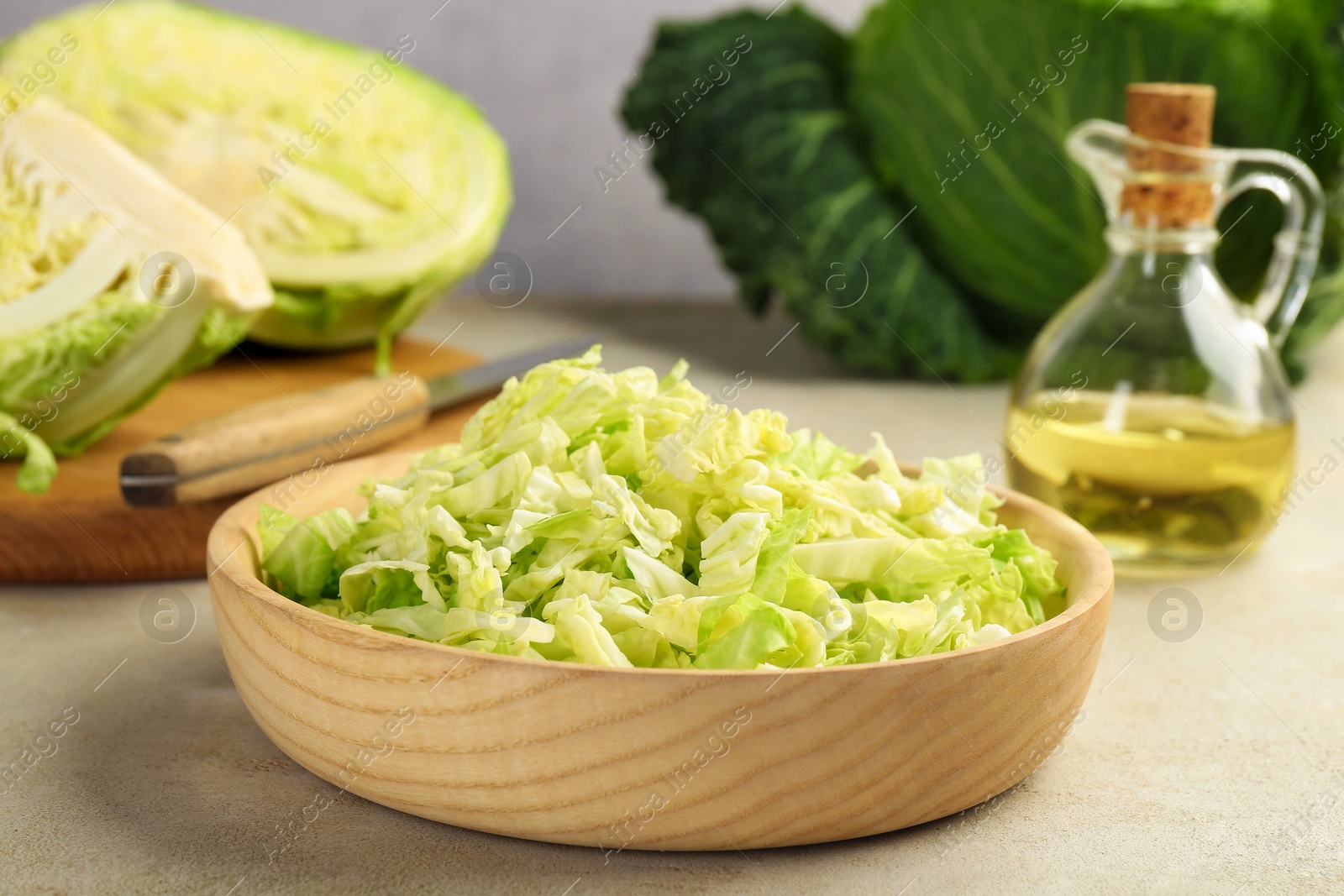 Photo of Shredded Savoy cabbage in bowl, knife and oil on light table, closeup