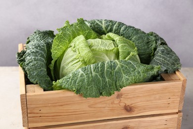 Photo of Fresh Savoy cabbage in wooden crate on grey table, closeup