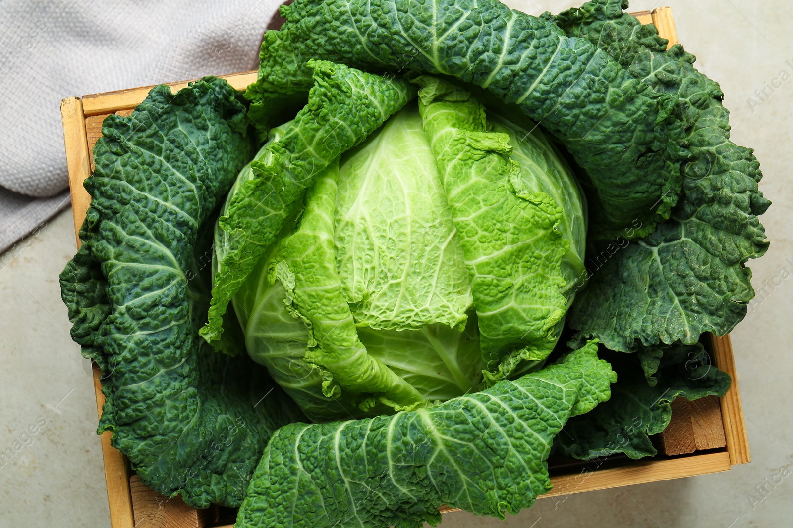 Photo of Fresh Savoy cabbage in wooden crate on light grey table, top view