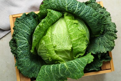 Photo of Fresh Savoy cabbage in wooden crate on light grey table, top view