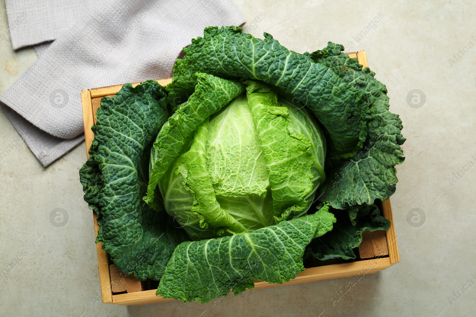 Photo of Fresh Savoy cabbage in wooden crate on light grey table, top view