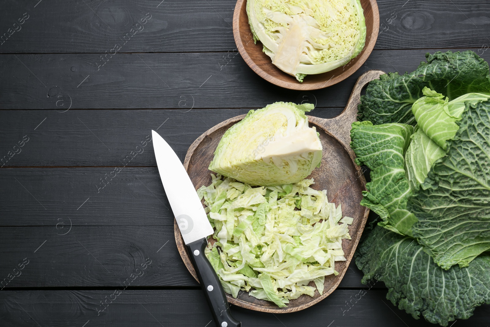 Photo of Fresh Savoy cabbages and knife on black wooden table, flat lay. Space for text
