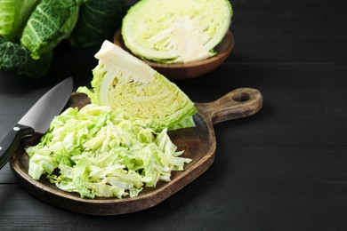 Photo of Fresh shredded Savoy cabbage and knife on black wooden table, closeup. Space for text