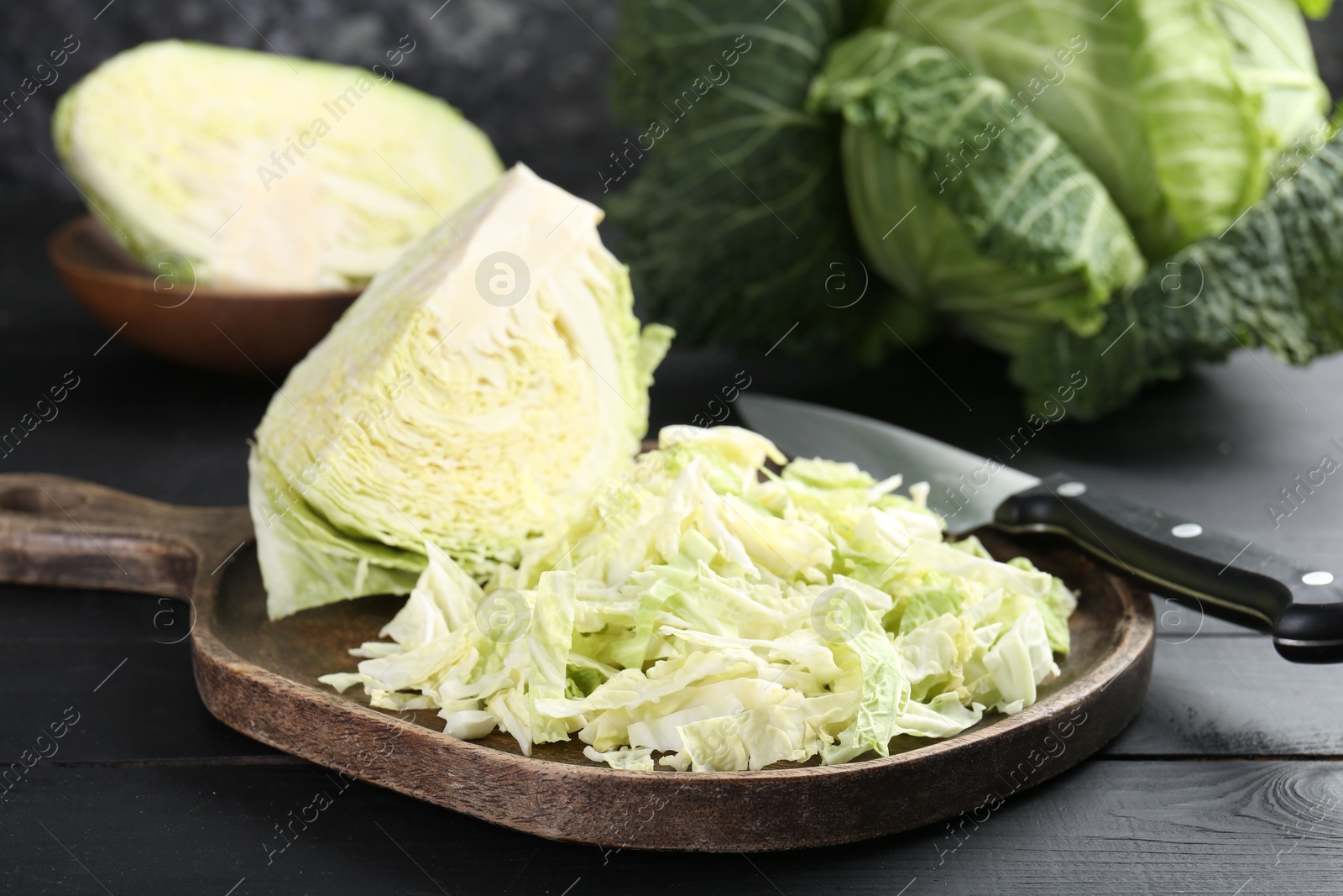 Photo of Fresh shredded Savoy cabbage and knife on black wooden table, closeup