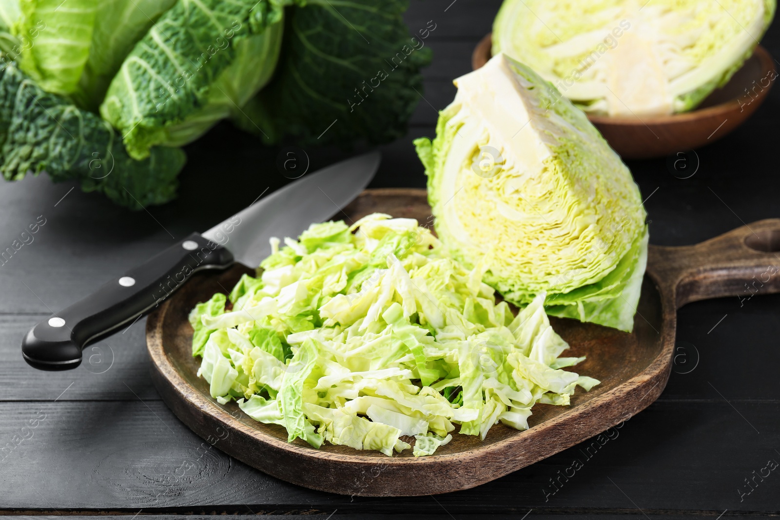 Photo of Fresh shredded Savoy cabbage and knife on black wooden table, closeup