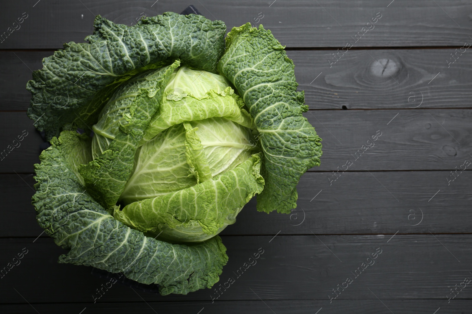 Photo of Fresh Savoy cabbage on black wooden table, top view. Space for text