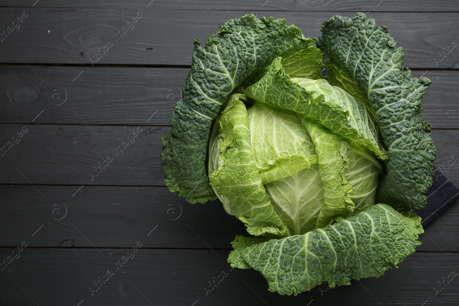 Photo of Fresh Savoy cabbage on black wooden table, top view. Space for text