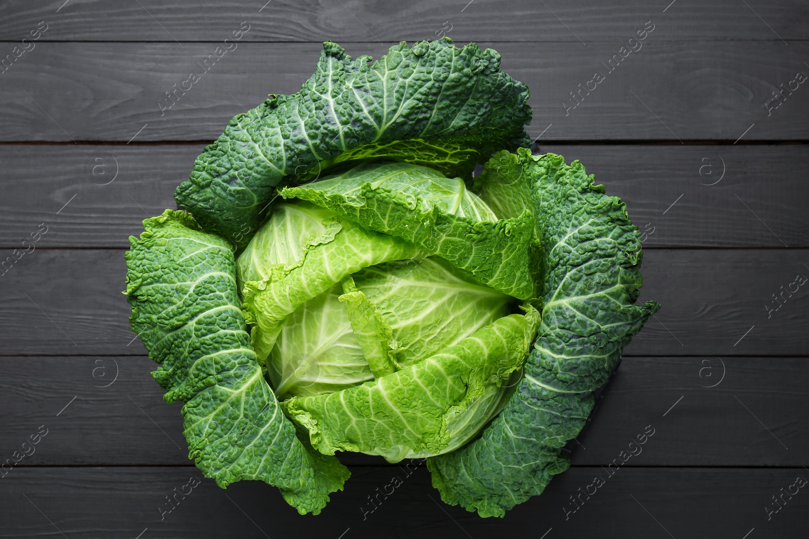 Photo of Fresh Savoy cabbage on black wooden table, top view
