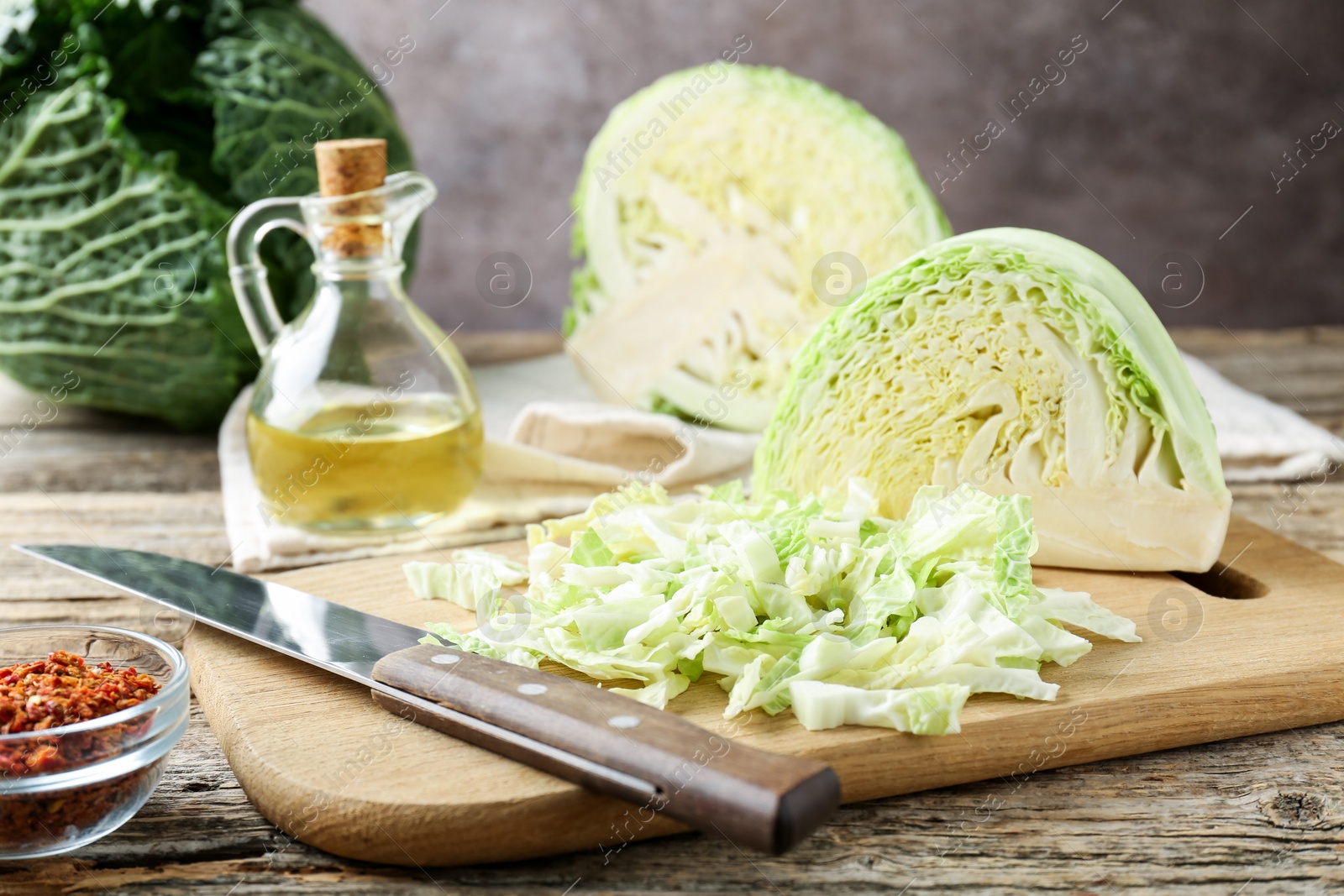 Photo of Cut fresh Savoy cabbages, knife, spices and oil on wooden table, closeup