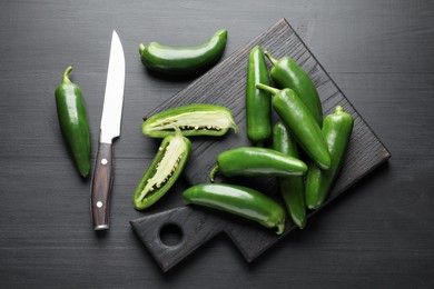 Photo of Fresh jalapeno peppers and knife on black wooden table, flat lay