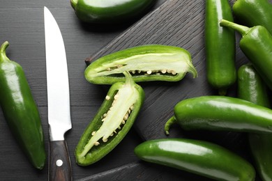 Photo of Fresh jalapeno peppers and knife on black wooden table, flat lay