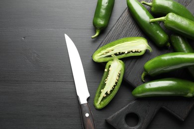 Photo of Fresh jalapeno peppers and knife on black wooden table, flat lay. Space for text