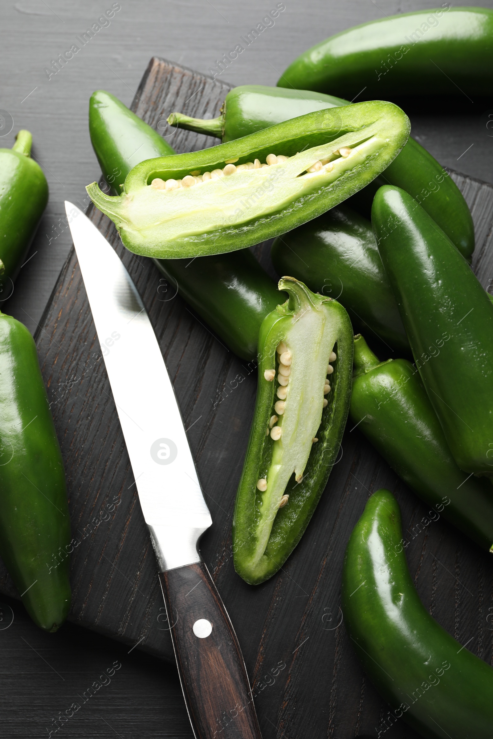 Photo of Fresh jalapeno peppers and knife on black wooden table, flat lay