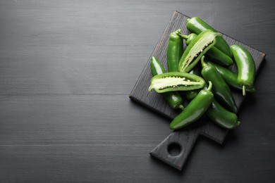 Photo of Fresh jalapeno peppers on black wooden table, top view. Space for text