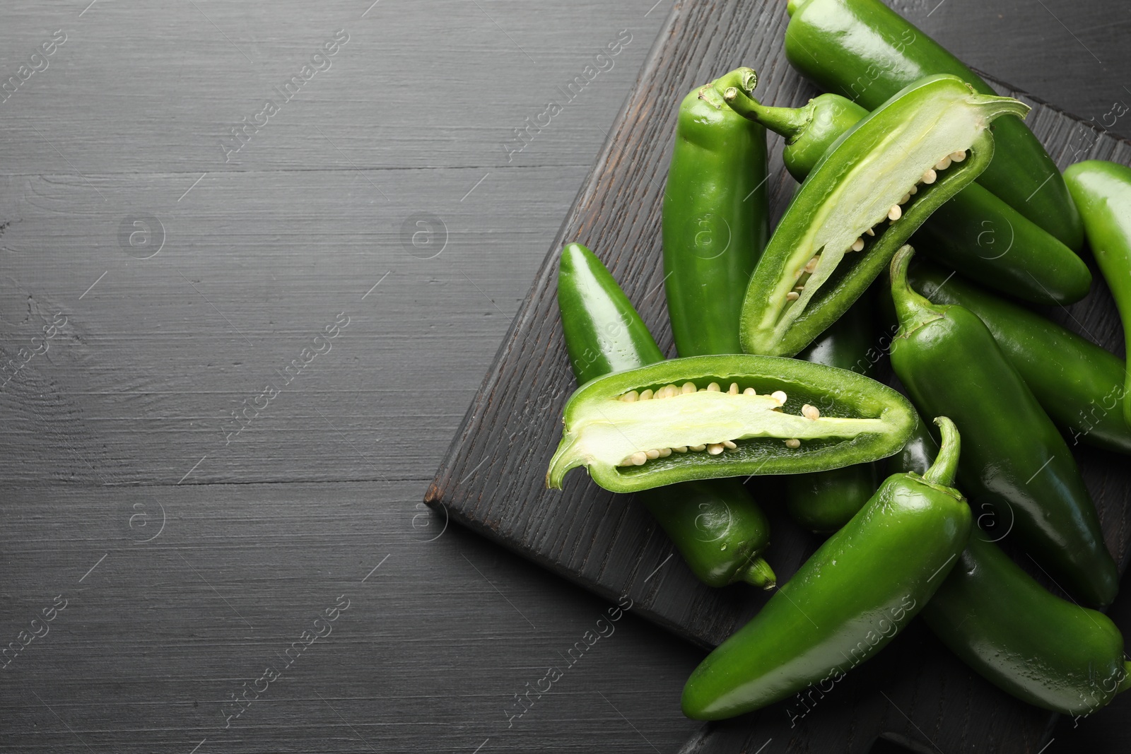 Photo of Fresh jalapeno peppers on black wooden table, top view. Space for text