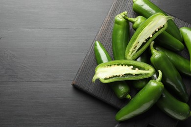 Photo of Fresh jalapeno peppers on black wooden table, top view. Space for text