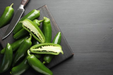 Photo of Fresh jalapeno peppers and knife on black wooden table, flat lay. Space for text