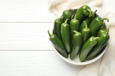 Photo of Fresh jalapeno peppers in bowl on white wooden table, above view. Space for text