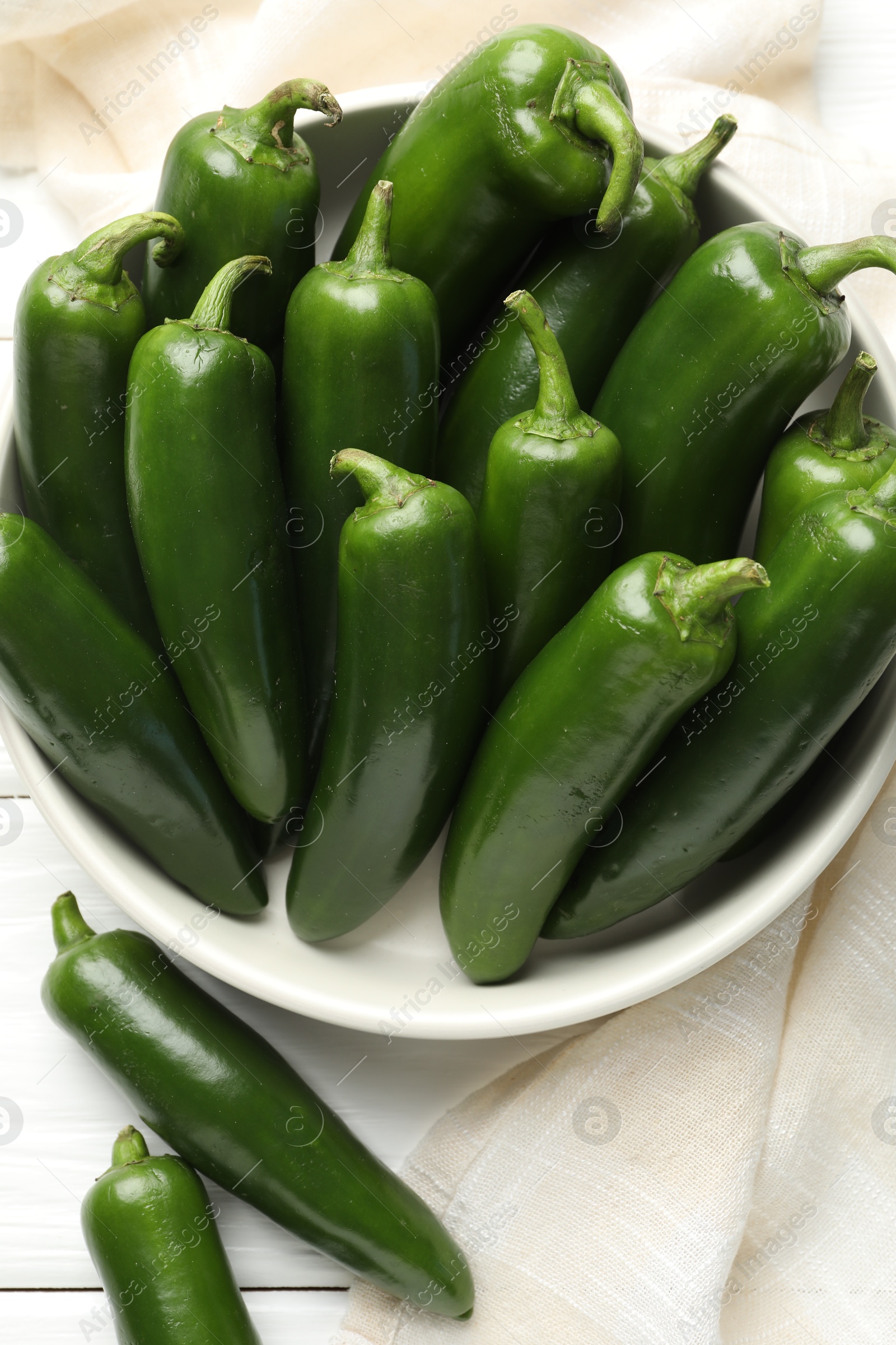 Photo of Fresh jalapeno peppers in bowl on white wooden table, above view