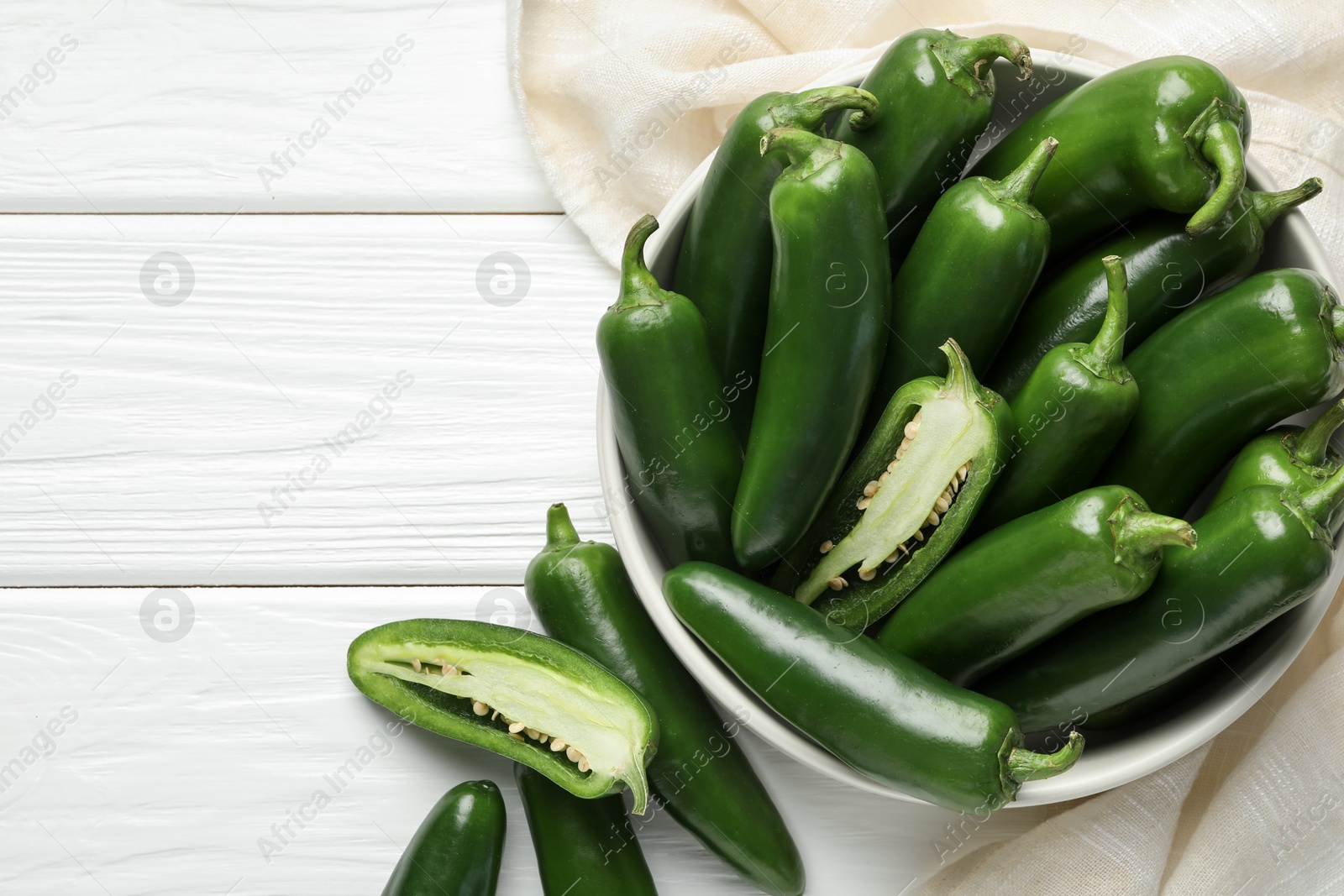 Photo of Fresh jalapeno peppers in bowl on white wooden table, above view. Space for text
