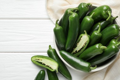 Photo of Fresh jalapeno peppers in bowl on white wooden table, above view. Space for text