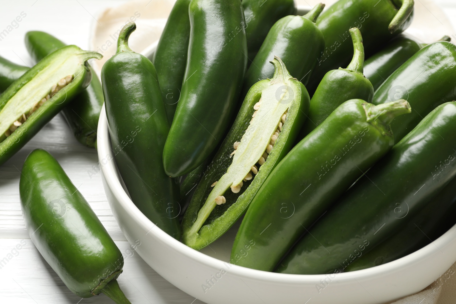 Photo of Fresh jalapeno peppers in bowl on white wooden table, closeup