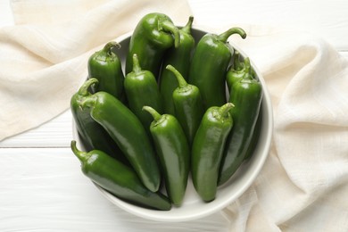 Photo of Fresh jalapeno peppers in bowl on white wooden table, above view