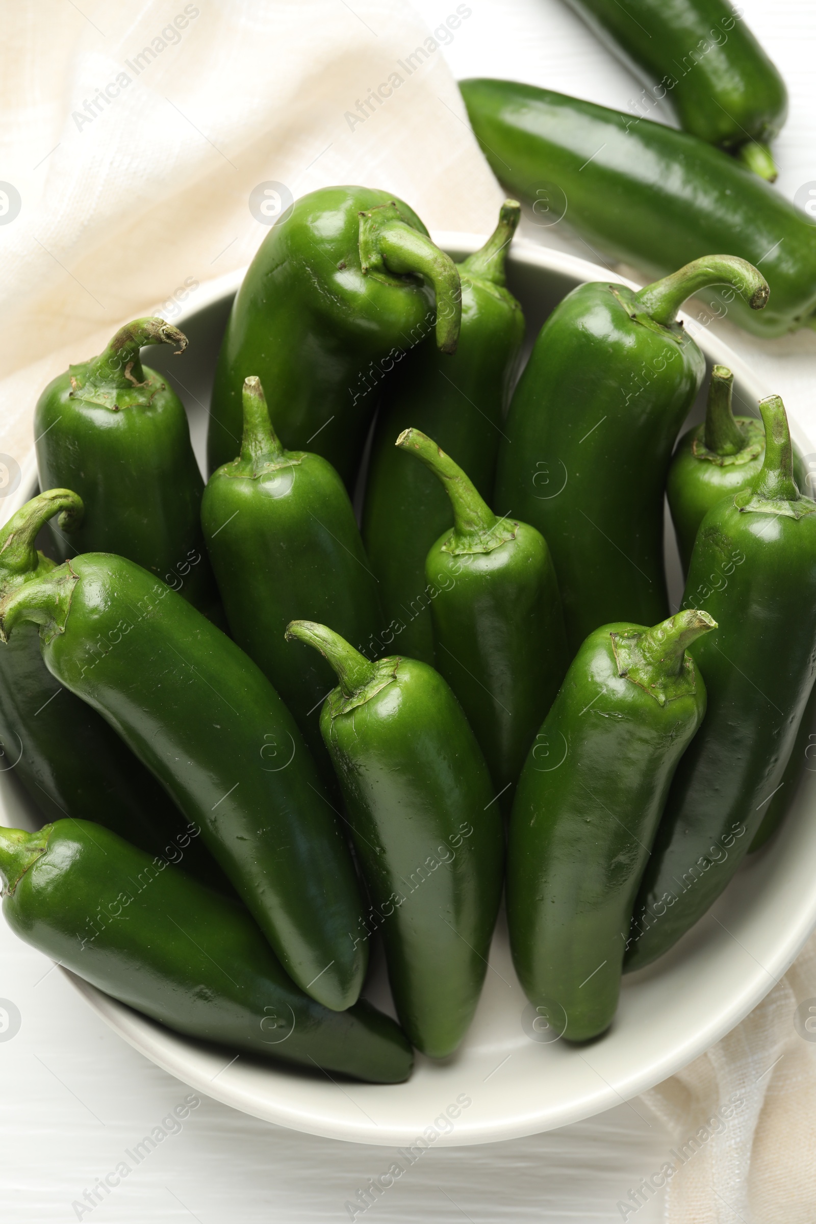Photo of Fresh jalapeno peppers in bowl on white wooden table, above view