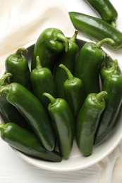 Photo of Fresh jalapeno peppers in bowl on white wooden table, above view