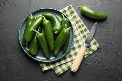 Photo of Fresh jalapeno peppers and knife on black textured table, flat lay