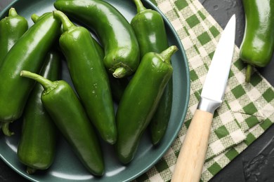 Photo of Fresh jalapeno peppers and knife on black table, above view