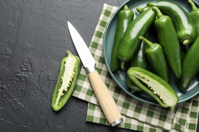 Photo of Fresh jalapeno peppers and knife on black textured table, flat lay